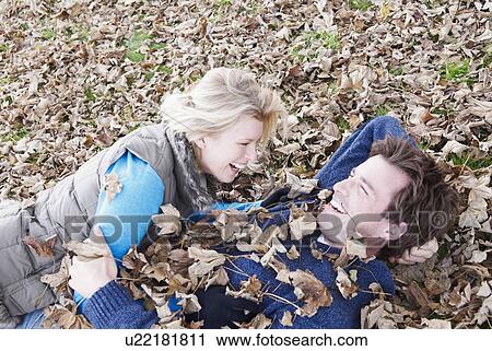Stock Image - Couple laughing, lying in leaves. Fotosearch
