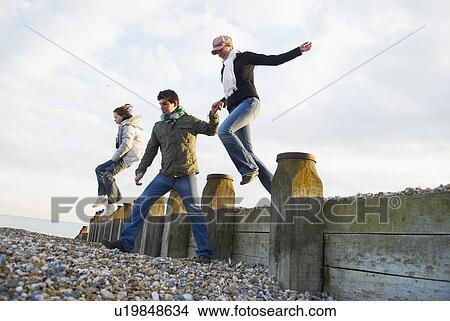 Picture - Family jump over breakwater on beach. Fotosearch