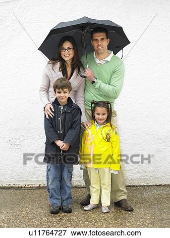 Stock Photo - Parents, boy (6-8) and girl (4-6) holding umbrellas, smiling. Fotosearch