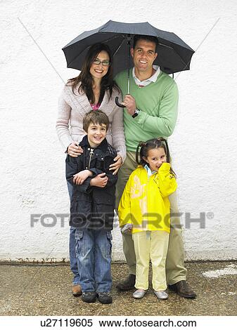 Parents, boy (6-8) and girl (4-6) sheltering under umbrella, smiling View Large Photo Image Stock Photography - Parents, boy (6-8) and girl (4-6) sheltering under umbrella, smiling. Fotosearch