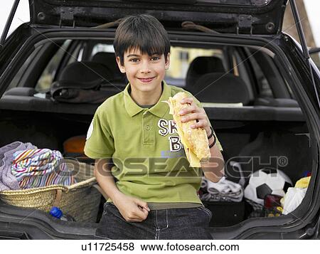 Boy (8-10) resting against open boot of parked car, eating baguette, portrait View Large Photo Image Stock Photo - Boy (8-10) resting against open boot of parked car, eating baguette, portrait. Fotosearch