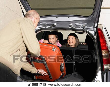 Stock Photo - Father loading luggage into car, children on backseat. Fotosearch