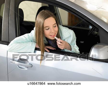 Picture - Girl (12-14) sitting in car applying lipstick in wing mirror. Fotosearch