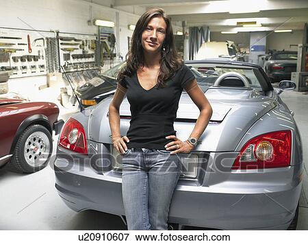Stock Photo - Woman leaning on a gray convertible in a garage.. Fotosearch