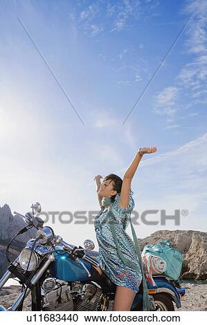 Stock Image - Woman on motorbike arms aloft. . Fotosearch