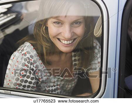 Stock Image - Woman sitting in car, looking through window, smiling, portrait. Fotosearch