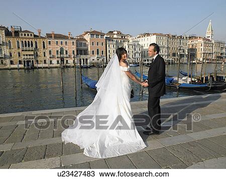 Stock Image - Bride and groom holding hands. Grand Canal, Venice, Italy.. Fotosearch