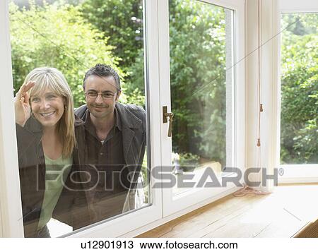 Stock Image - Close up of couple looking through window into empty house.. Fotosearch