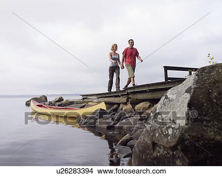 Couple holding hands walking on a dock near a boat smiling. View Large Photo Image Picture - Couple holding hands walking on a dock near a boat smiling.. Fotosearch