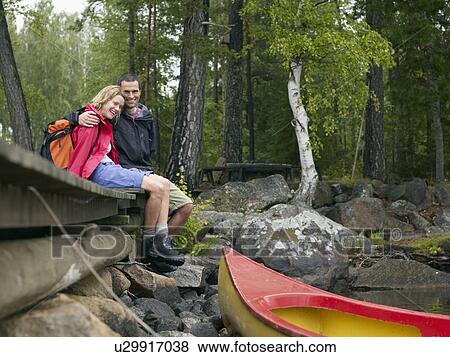 Stock Photo - Couple sitting on a dock near a boat laughing.. Fotosearch