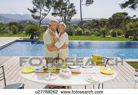 Stock Image - Man and woman embracing by poolside.. Fotosearch