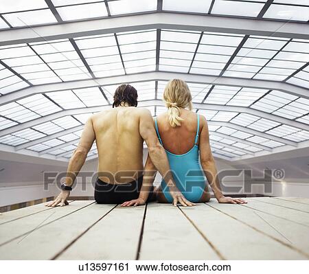 Stock Image - Mature couple sitting on decking indoors, rear view. Fotosearch