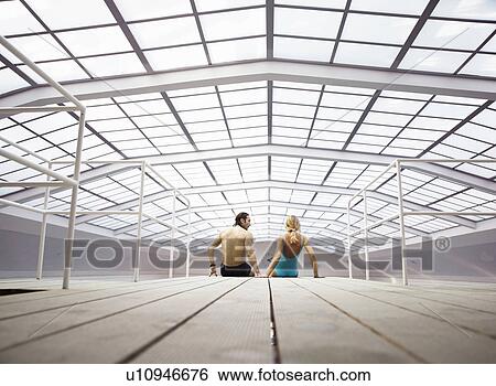 Stock Photograph - Mature couple sitting on decking indoors, rear view. Fotosearch