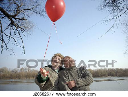 Senior couple by river holding red balloon, smiling View Large Photo Image Stock Photo - Senior couple by river holding red balloon, smiling. Fotosearch