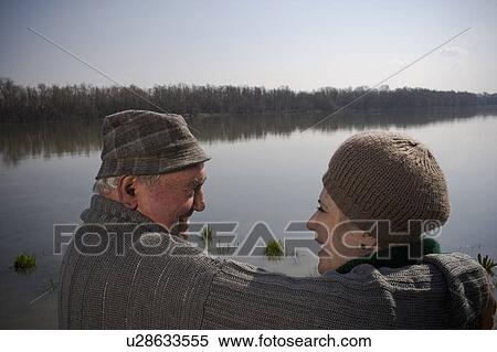Stock Photography - Senior couple by river, man holding arm around woman, rear view. Fotosearch