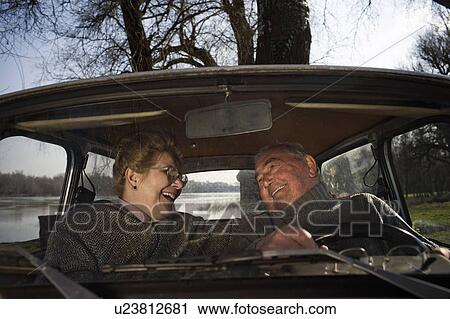 Stock Image - Senior couple sitting in car, smiling at each other. Fotosearch