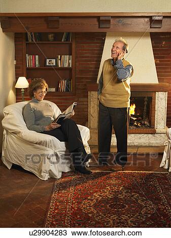 Stock Image - Senior man using mobile phone, woman reading, smiling. Fotosearch