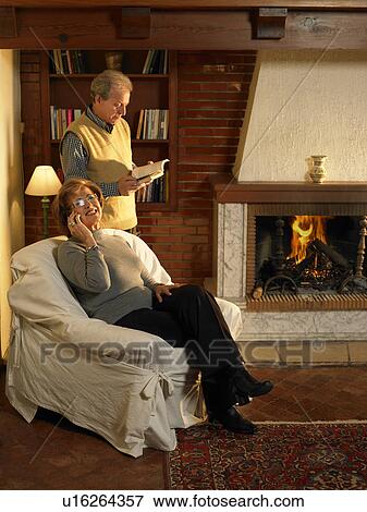 Stock Photo - Senior woman using mobile phone, man reading in background. Fotosearch