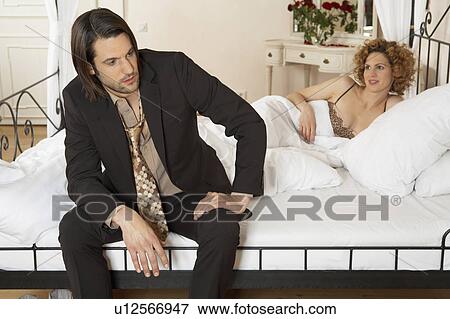 Young Businessman Sitting On Bed With Woman Lying In Bed In Background Stock Photo U Fotosearch