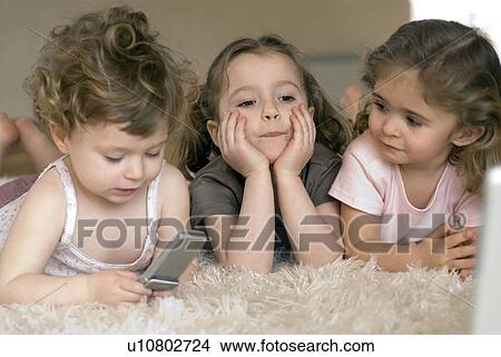 Picture - Three little girls (9-12 months, 2-4 ) using mobile phone and laptop.. Fotosearch