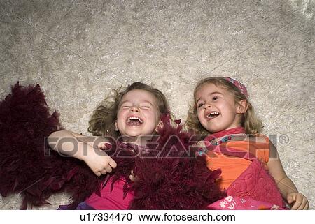 Stock Image - Two girls (2-4) dressed for a party, lying on rug.. Fotosearch
