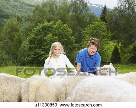 Stock Photo - Young boy and young girl smiling and feeding sheep in a field.. Fotosearch