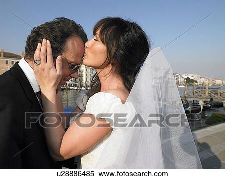 Stock Photography - Bride kissing groom's forehead. Grand Canal, Venice, Italy.. Fotosearch