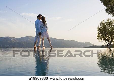 Stock Photograph - Couple kissing and holding hands by infinity pool.. Fotosearch