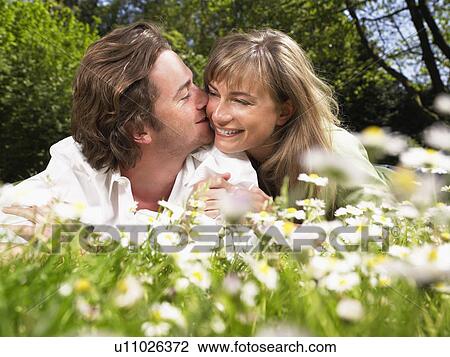 Stock Image - Couple lying in the grass smiling and kissing.. Fotosearch