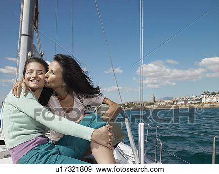 Stock Photo - Mature mother kissing daughter on yacht, smiling. Fotosearch