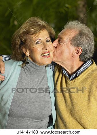 Stock Image - Senior woman being kissed by senior man, smiling, portrait. Fotosearch