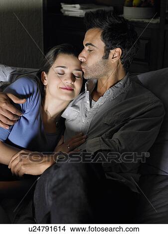 Picture - Young couple relaxing on sofa, man kissing woman. Fotosearch