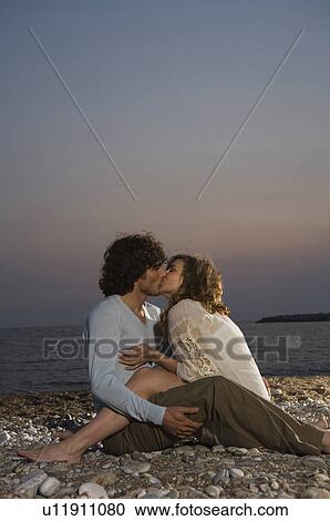 Young couple sitting on beach kissing, sunset View Large Photo Image Stock Image - Young couple sitting on beach kissing, sunset. Fotosearch