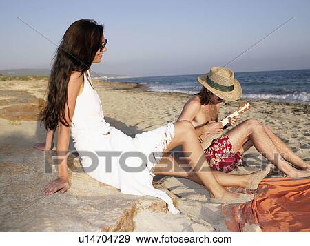 Man playing a ukulele on the beach while a smiling woman watches. View Large Photo Image Stock Photo - Man playing a ukulele on the beach while a smiling woman watches.. Fotosearch