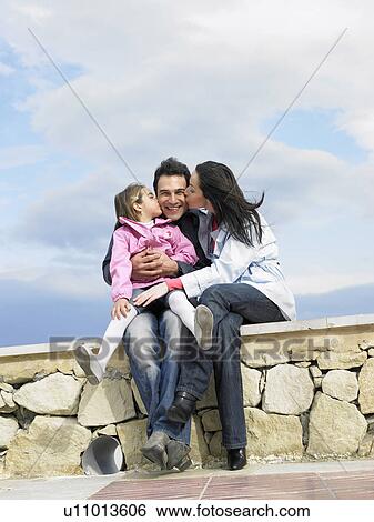 Mother and daughter (6-8) kissing father on beach wall View Large Photo Image Stock Photograph - Mother and daughter (6-8) kissing father on beach wall. Fotosearch