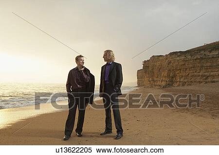 Stock Photography - Two men standing on beach at sunset.. Fotosearch