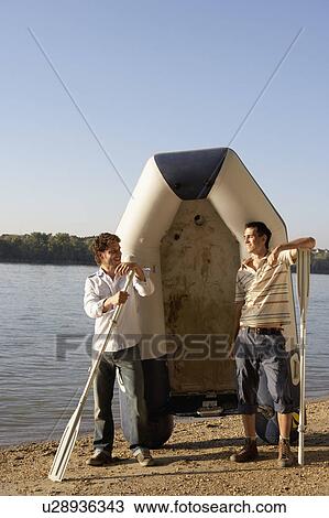 Stock Image - Two men with oars and a raft on a beach smiling.. Fotosearch