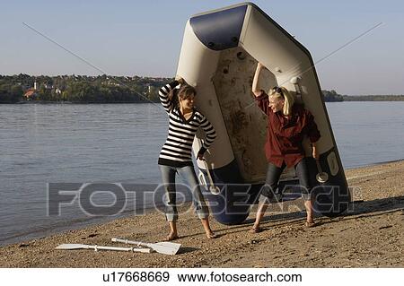 Two women carrying a raft on a beach smiling. View Large Photo Image Stock Photo - Two women carrying a raft on a beach smiling.. Fotosearch
