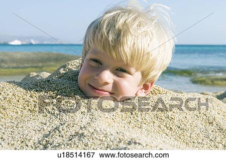 Stock Photo - Young boy buried in the sand smiling.. Fotosearch