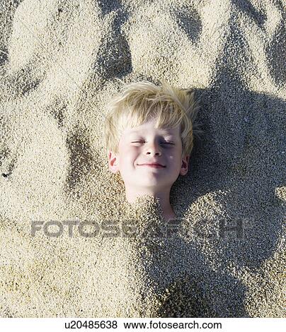 Stock Photo - Young boy buried in the sand smiling.. Fotosearch