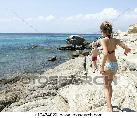 Young girl and young boy walking on rocks by the water. View Large Photo Image Stock Image - Young girl and young boy walking on rocks by the water.. Fotosearch