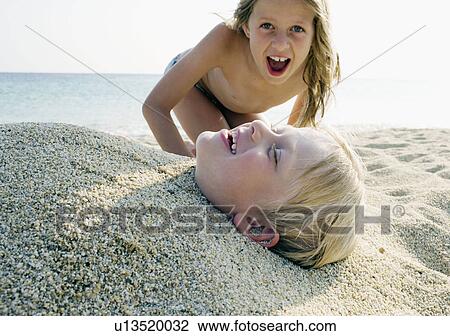 Young girl burying young boy in the sand at the beach. View Large Photo Image Stock Image - Young girl burying young boy in the sand at the beach.. Fotosearch