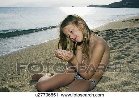 Young girl sitting on the beach holding a seashell. View Large Photo Image Stock Image - Young girl sitting on the beach holding a seashell.. Fotosearch