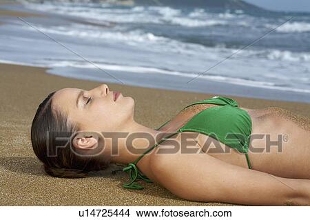 Young woman in bikini on beach lying in sand eyes closed sea in background. View Large Photo Image Picture - Young woman in bikini on beach lying in sand eyes closed sea in background.. Fotosearch