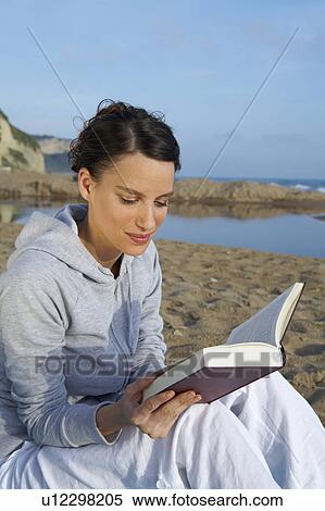 Stock Photography - Young woman on beach portrait reading a book sea and sky in background.. Fotosearch