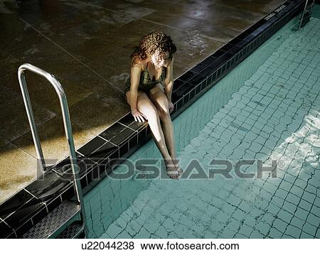 Stock Photo - Woman sitting by swimming pool, elevated view. Fotosearch