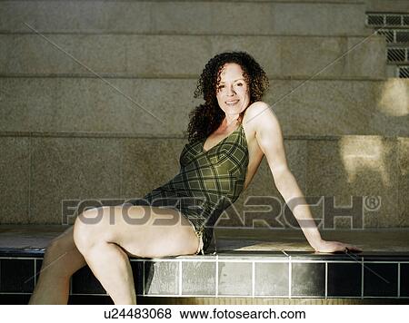 Stock Photo - Woman sitting by swimming pool, smiling, portrait. Fotosearch