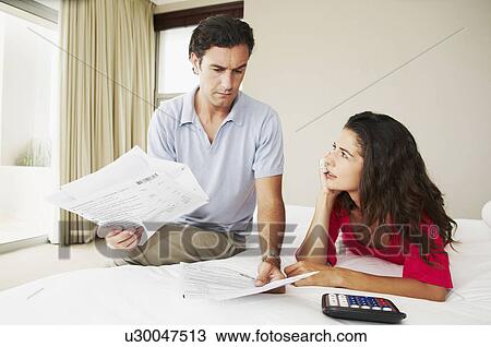 Stock Image - Couple discuss bills on bed. Fotosearch