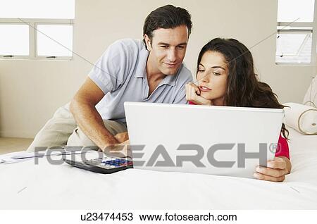 Stock Image - Couple discussing bills on bed. Fotosearch
