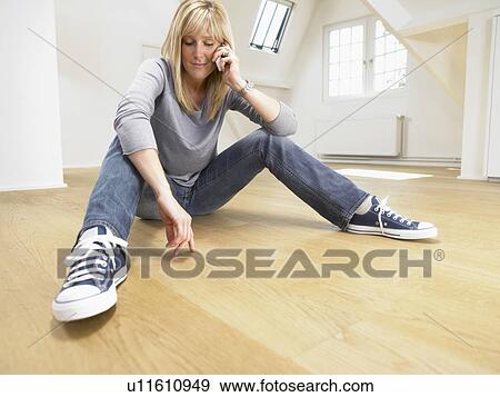 Relaxed woman seated on wooden floor giving a call with her cellular. White empty loft. View Large Photo Image Stock Photo - Relaxed woman seated on wooden floor giving a call with her cellular. White empty loft.. Fotosearch